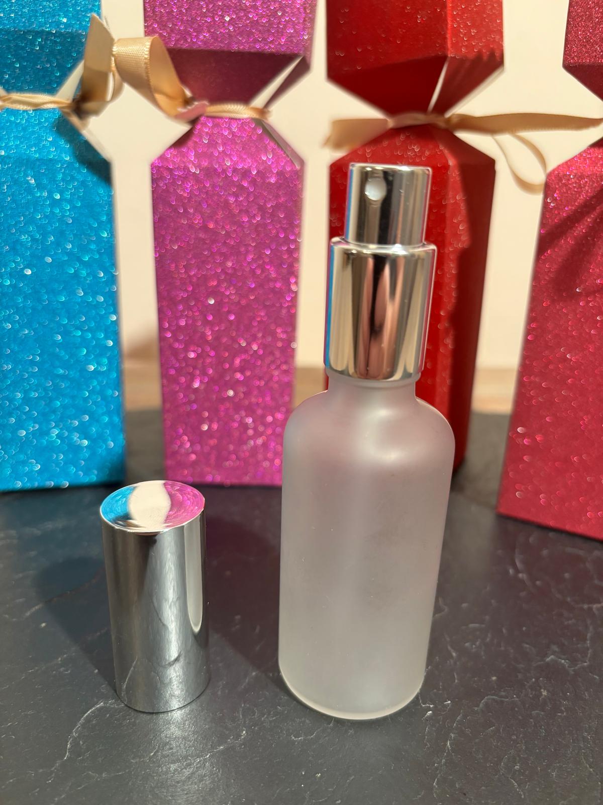 Frosted spray bottle with silver cap on a dark surface with colorful gift boxes in the background.
